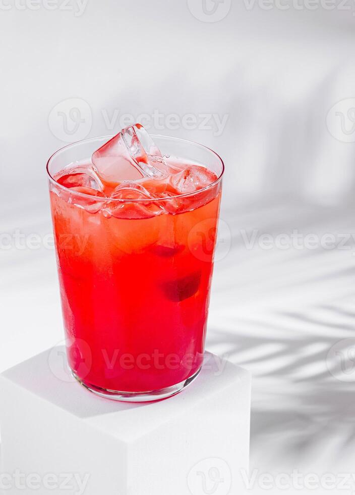 Red cocktail standing on white cube with palm leaf shadow photo