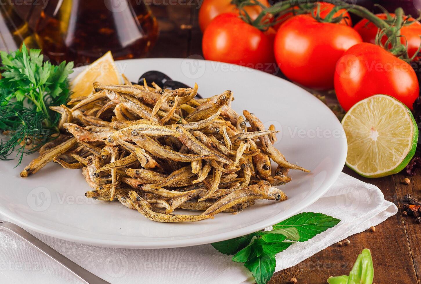 Fried anchovies served on white plate with herbs and spices on rustic wooden table photo
