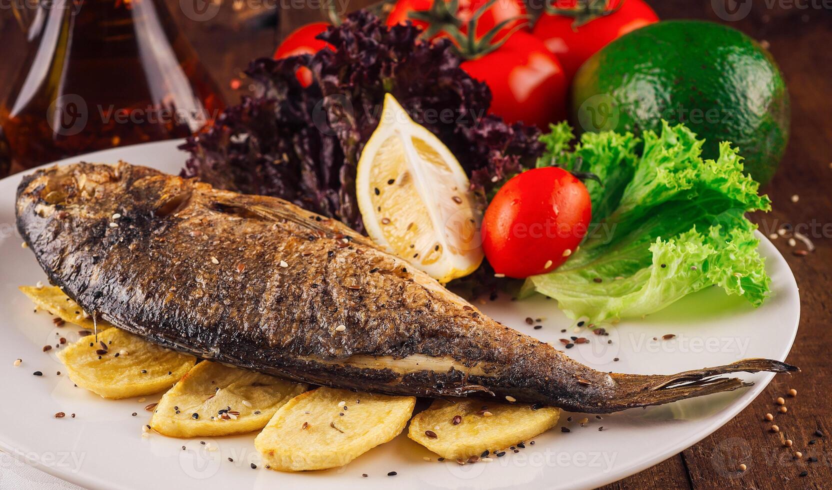 Grilled fish with potatoes and vegetables on white plate being served on wooden table photo