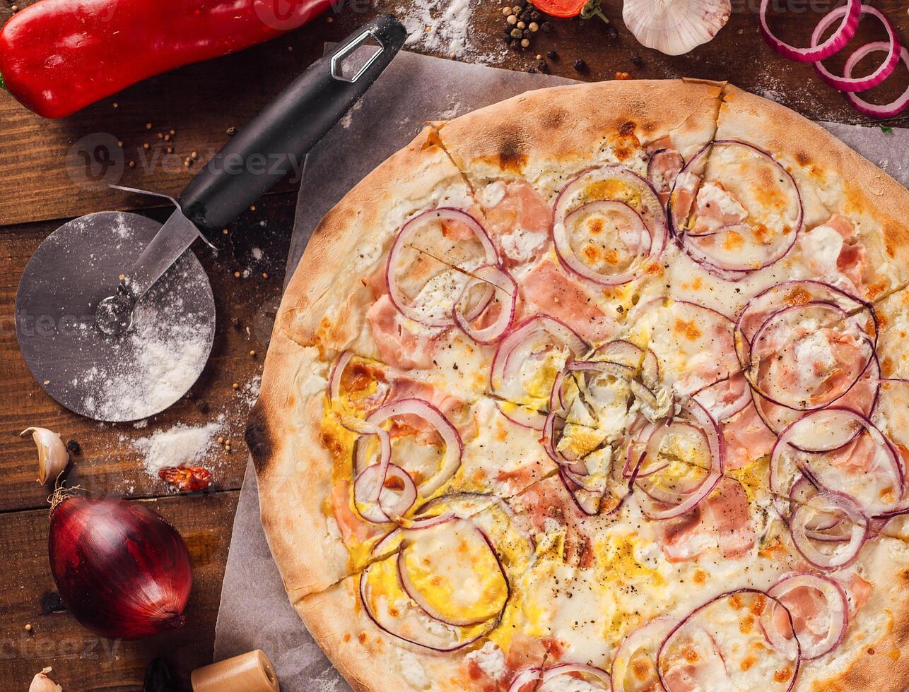 Delicious pizza lying on wooden table surrounded by fresh ingredients photo