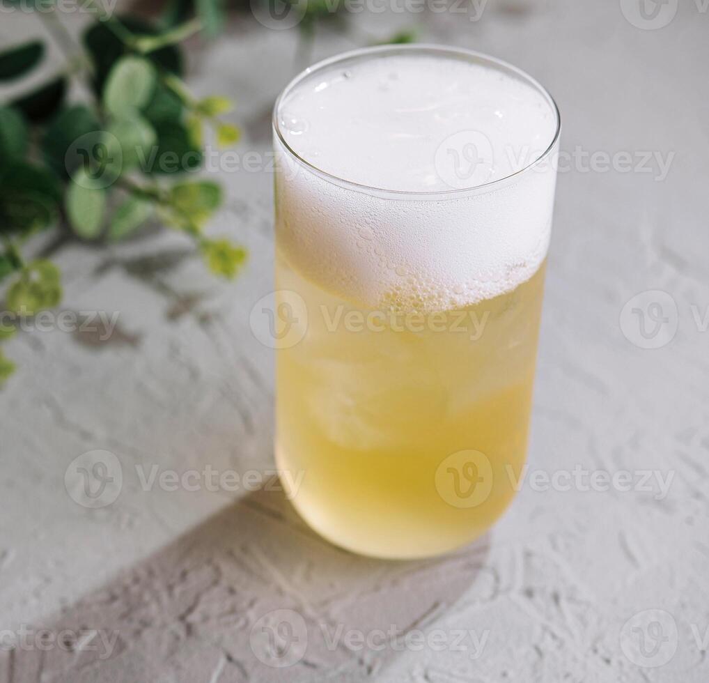 Glass of cold cocktail with foam on white table background with green leaves photo