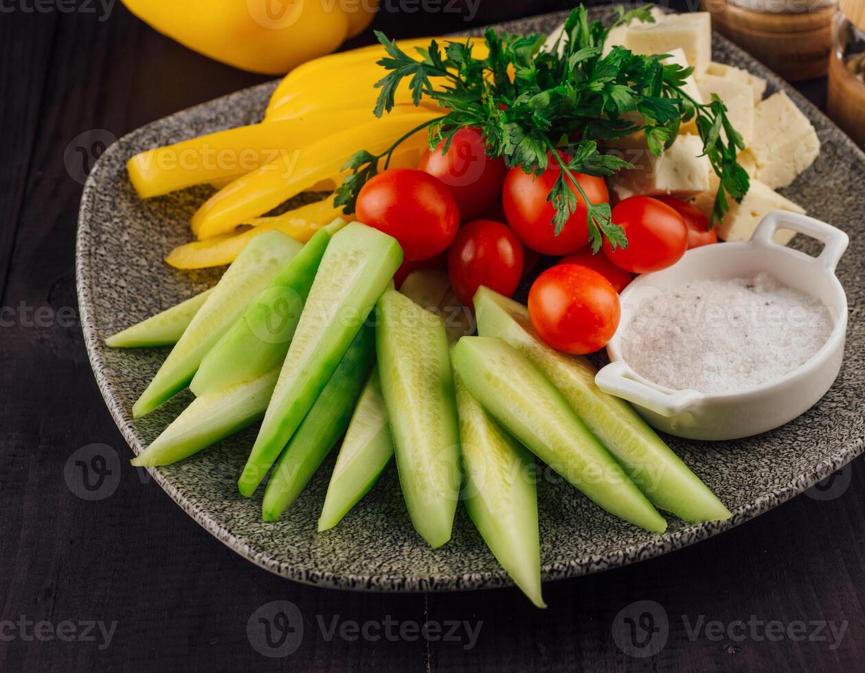 Plate presenting sliced cucumbers, tomatoes, cheese and peppers with spices aside photo