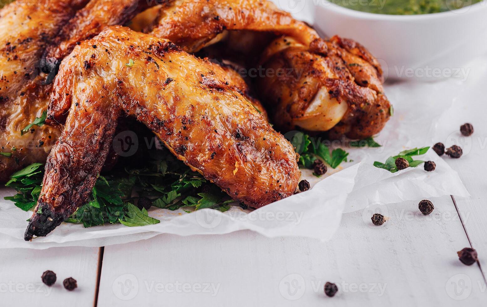 Delicious roasted chicken wings lying on white paper on white table photo