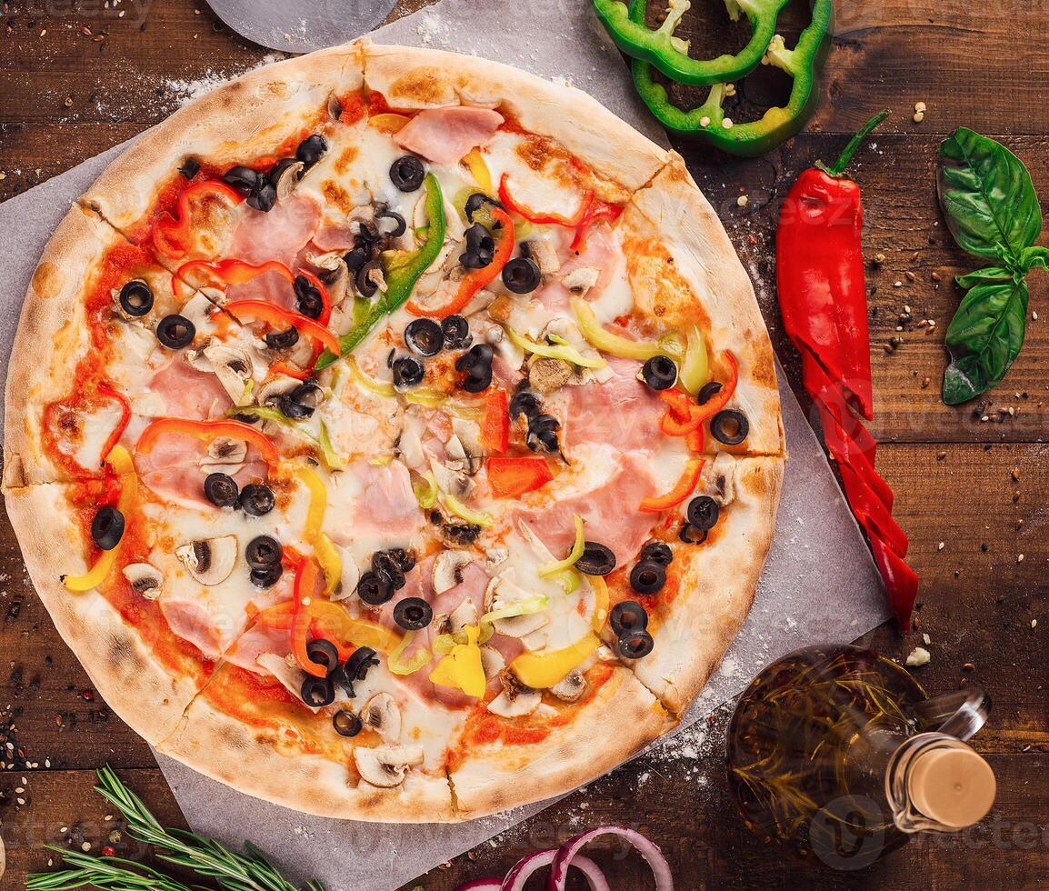 Delicious pizza lying on wooden table surrounded by fresh ingredients photo