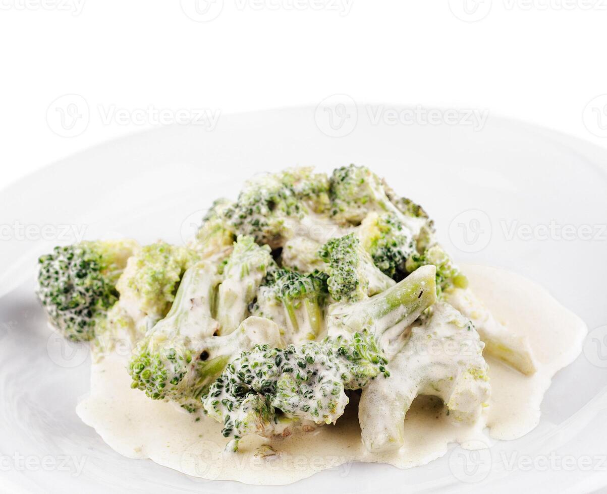 Steamed broccoli florets covered with creamy cheese sauce on white plate photo