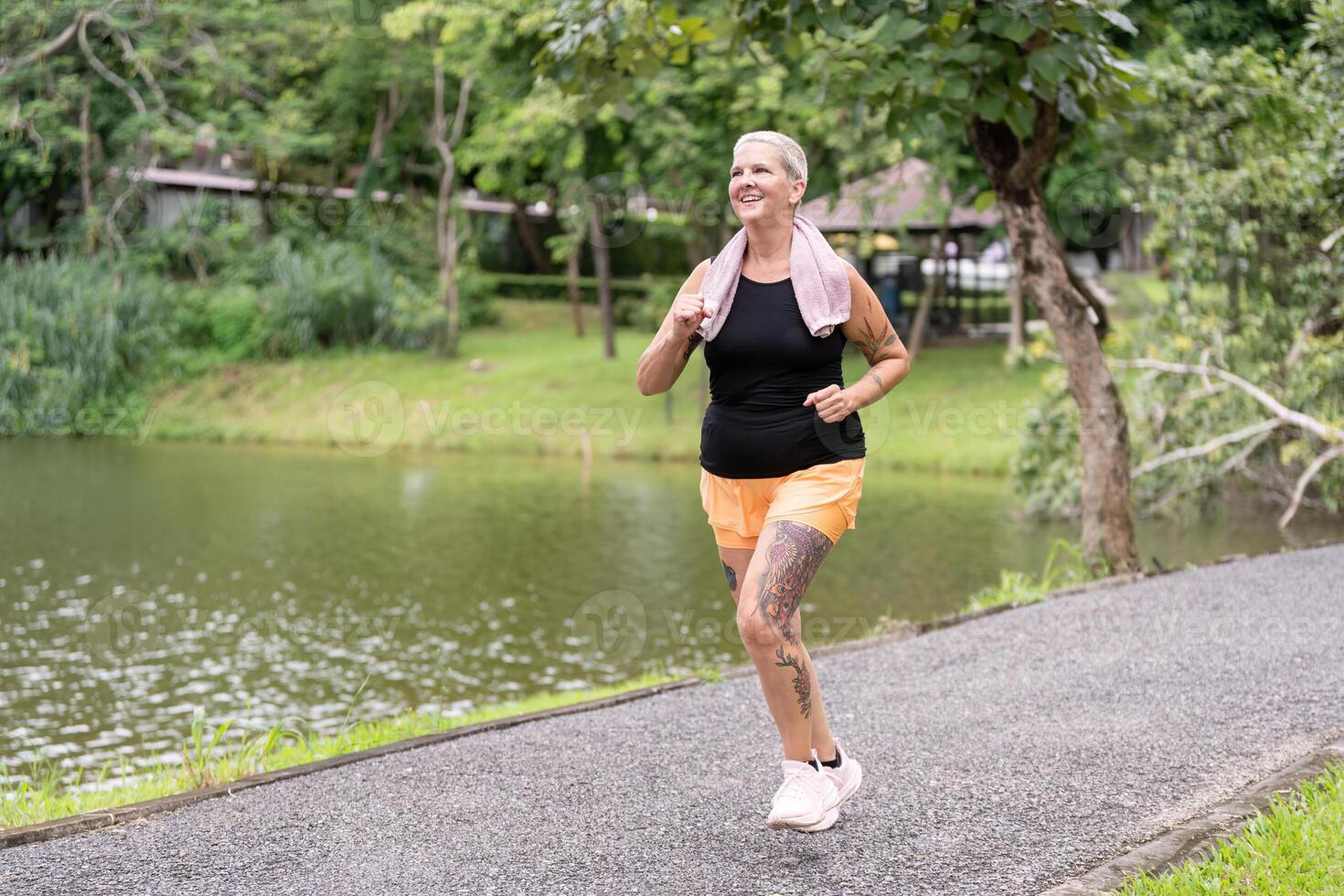 Active Senior Woman Jogging Outdoors in a Park with a Lake and Trees in the Background photo