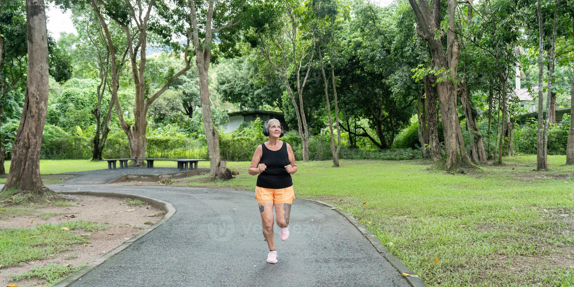Senior Woman Jogging in a Lush Green Park on a Paved Pathway Surrounded by Trees and Nature photo