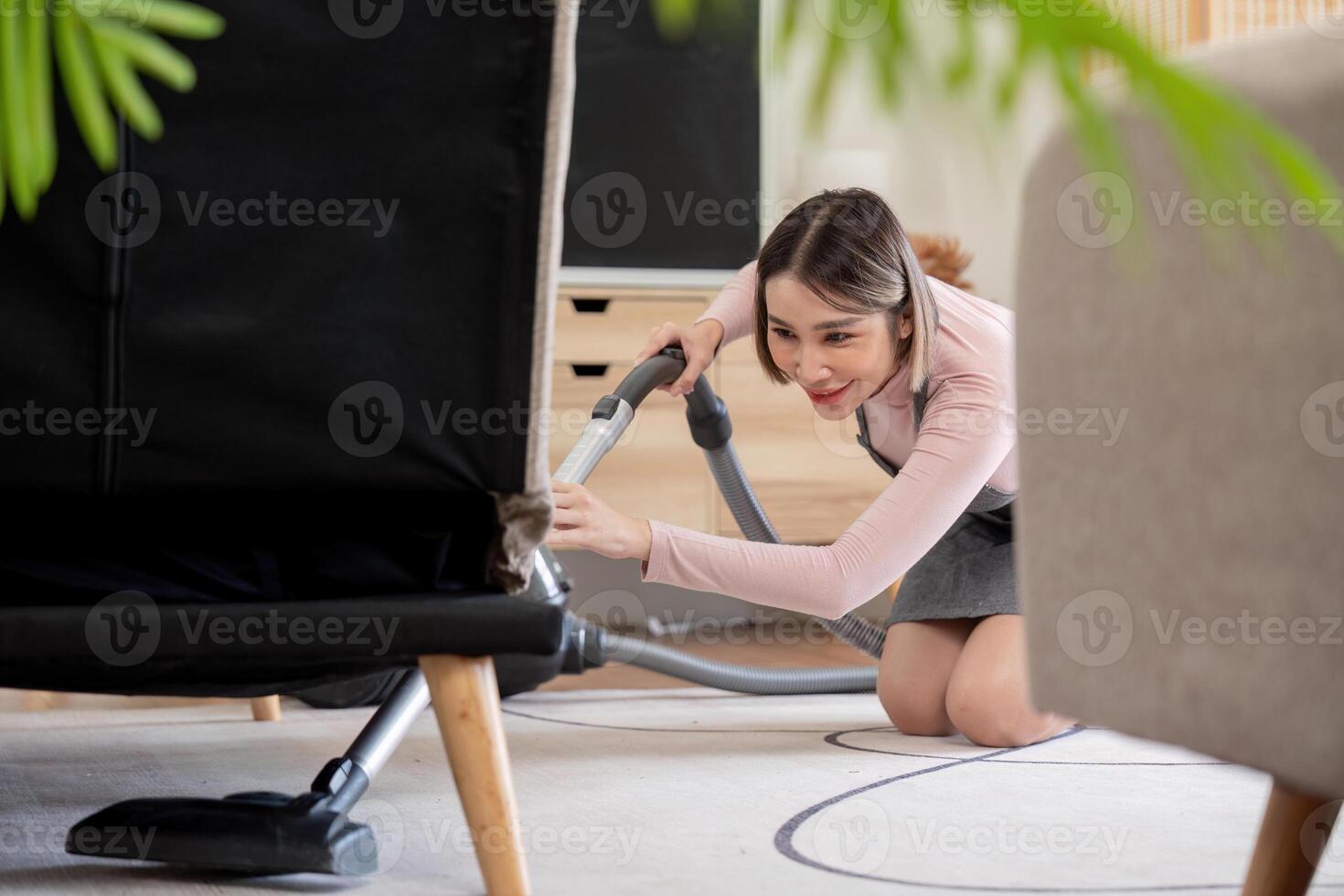 Housekeeper vacuuming under furniture in living room photo