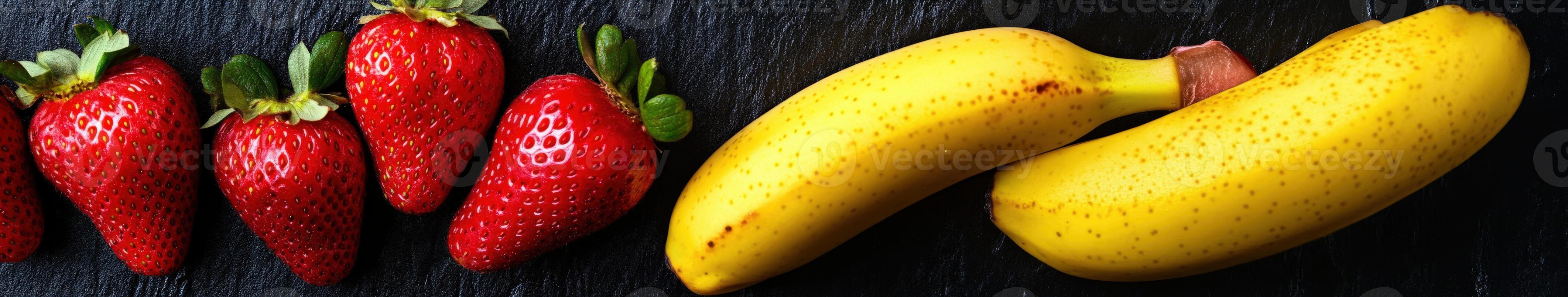 Fresh strawberries and ripe bananas arranged on a black surface photo