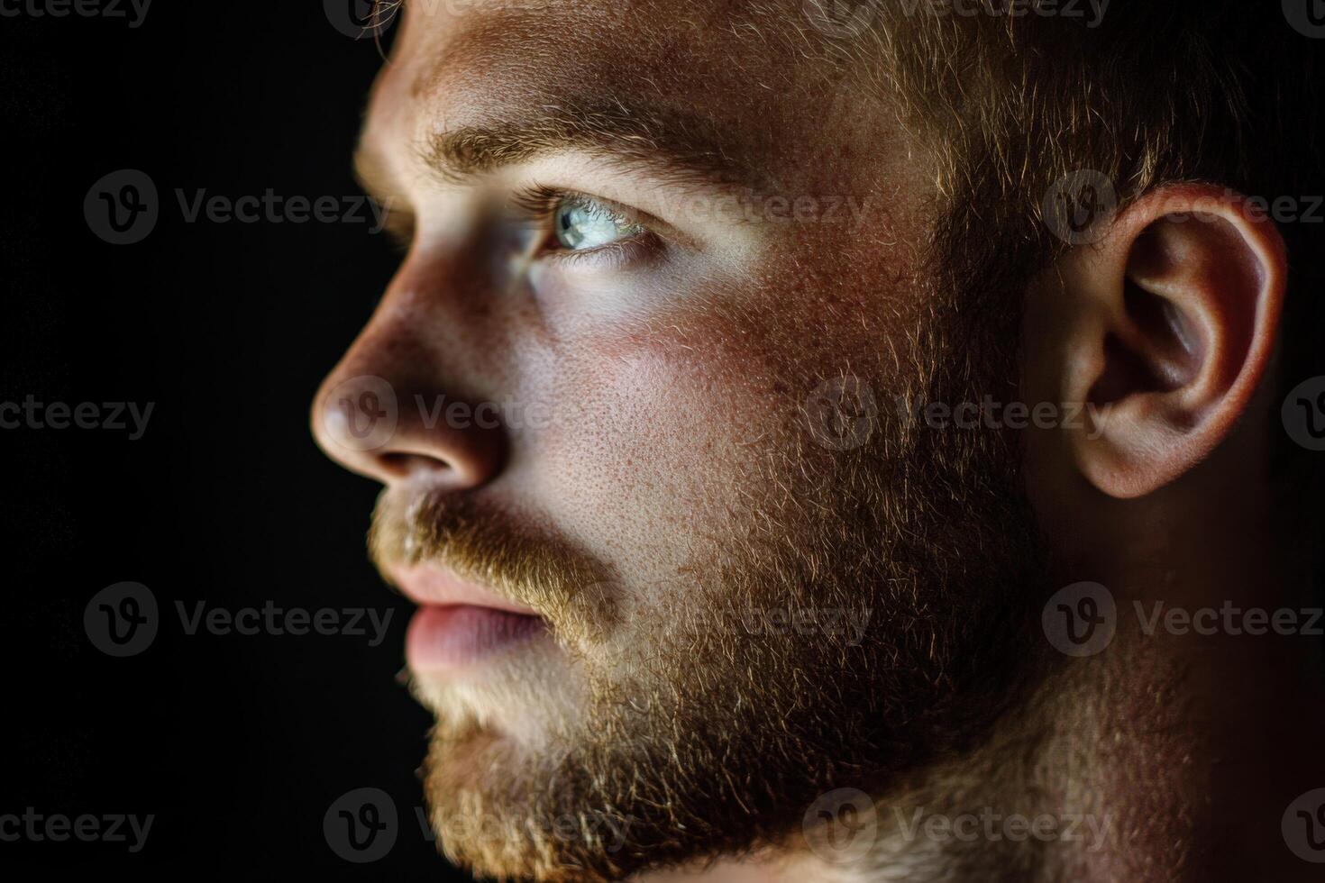 Close-up of a young man with a beard gazing thoughtfully in low light photo