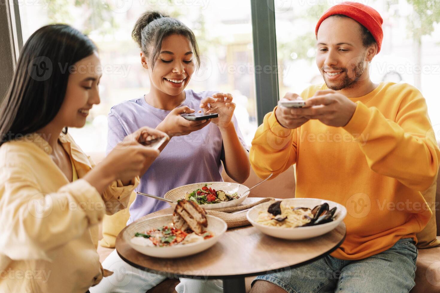 Happy diverse friends taking photos of food using smartphones in restaurant