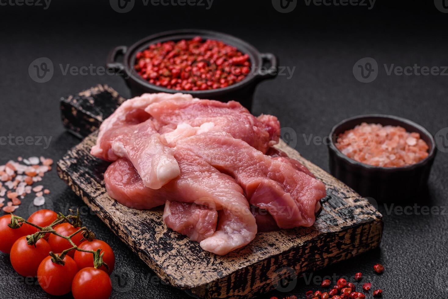A pieces of raw fresh pork on a wooden cutting board with spices and herbs photo