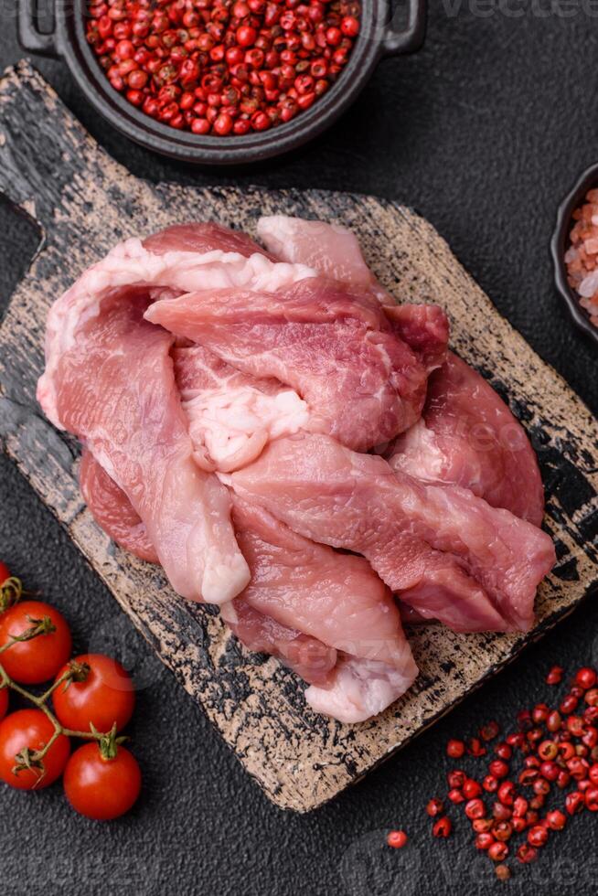 A pieces of raw fresh pork on a wooden cutting board with spices and herbs photo