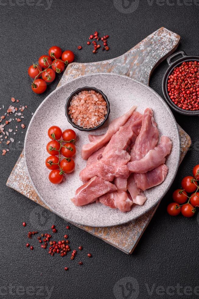 A pieces of raw fresh pork on a wooden cutting board with spices and herbs photo
