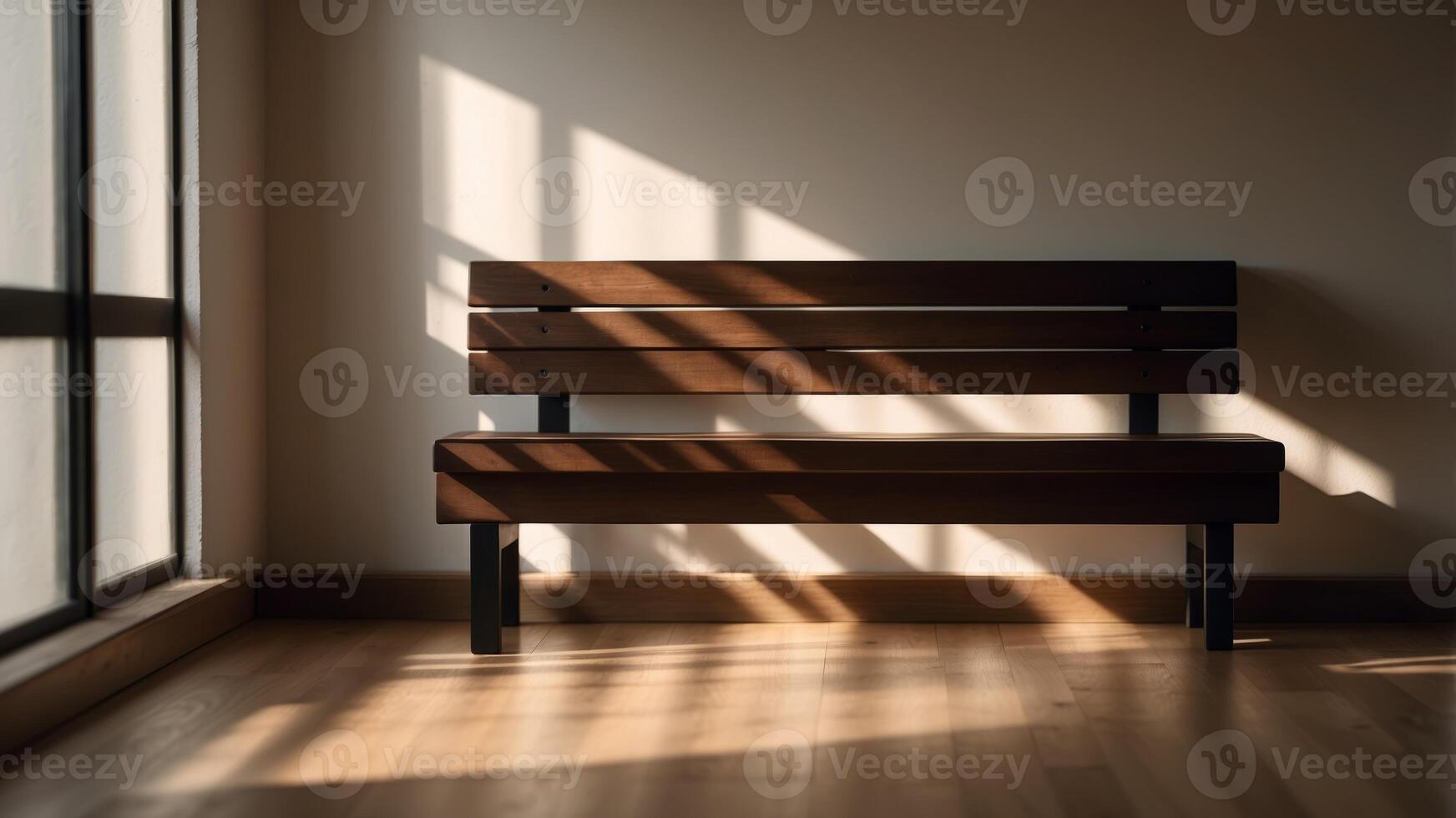 A simple brown bench sits in a room with sunlight streaming through the window, casting long shadows on the wall. photo