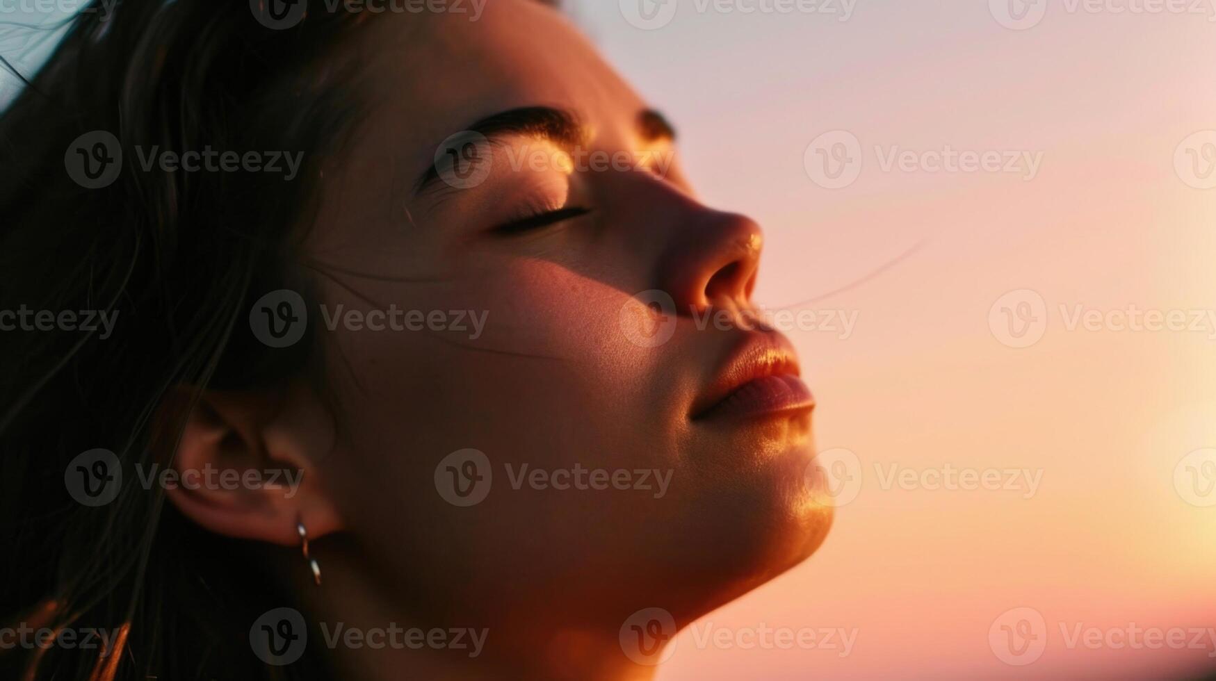 A serene portrait of a woman with her face tilted towards the sky, capturing the soft pink hues of the sunrise on her skin. photo