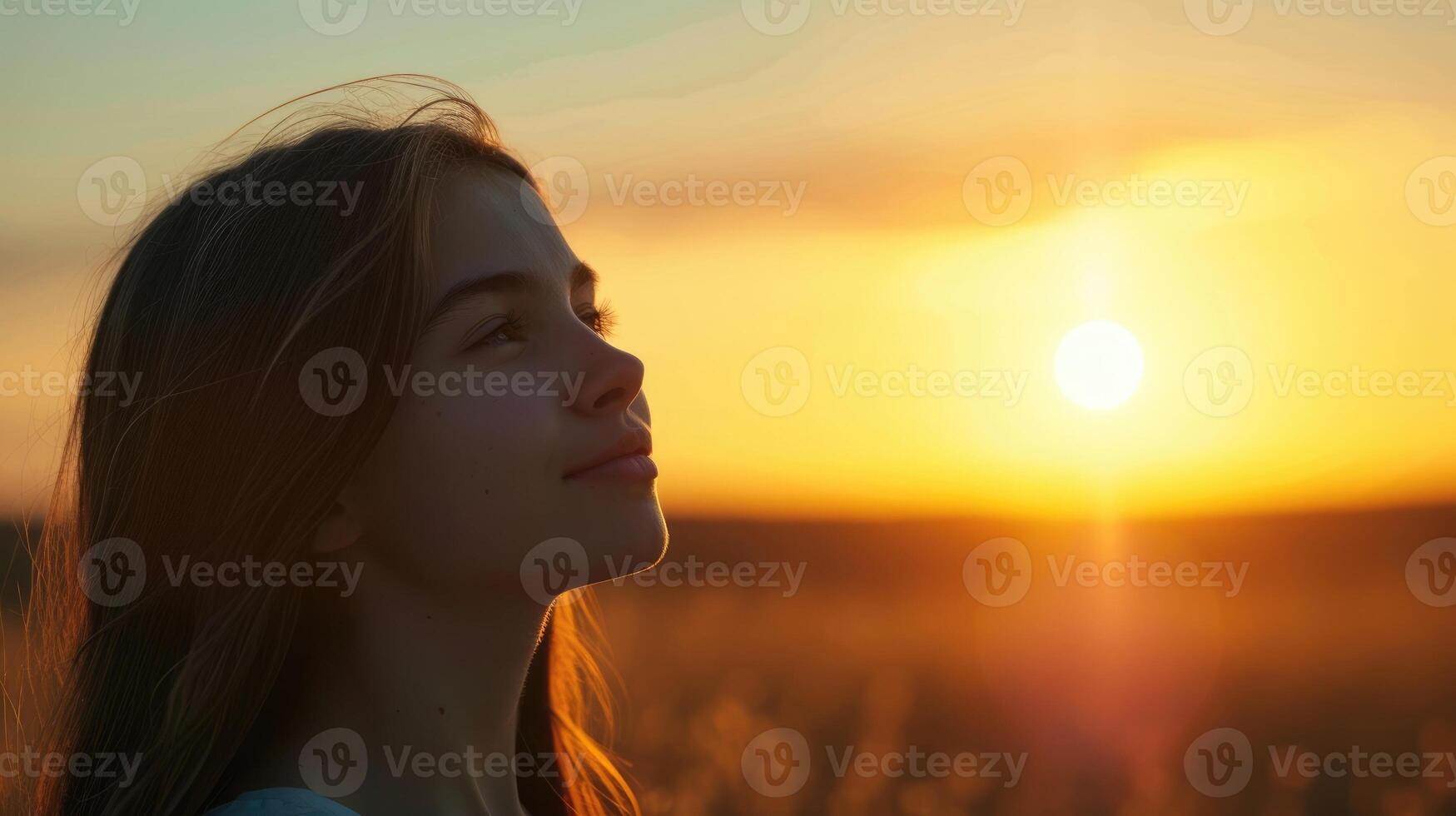 A teenage girl her eyes wide open and a small smile on her face as she gazes at a beautiful sunset and reflects on the beauty and vastness of the universe photo