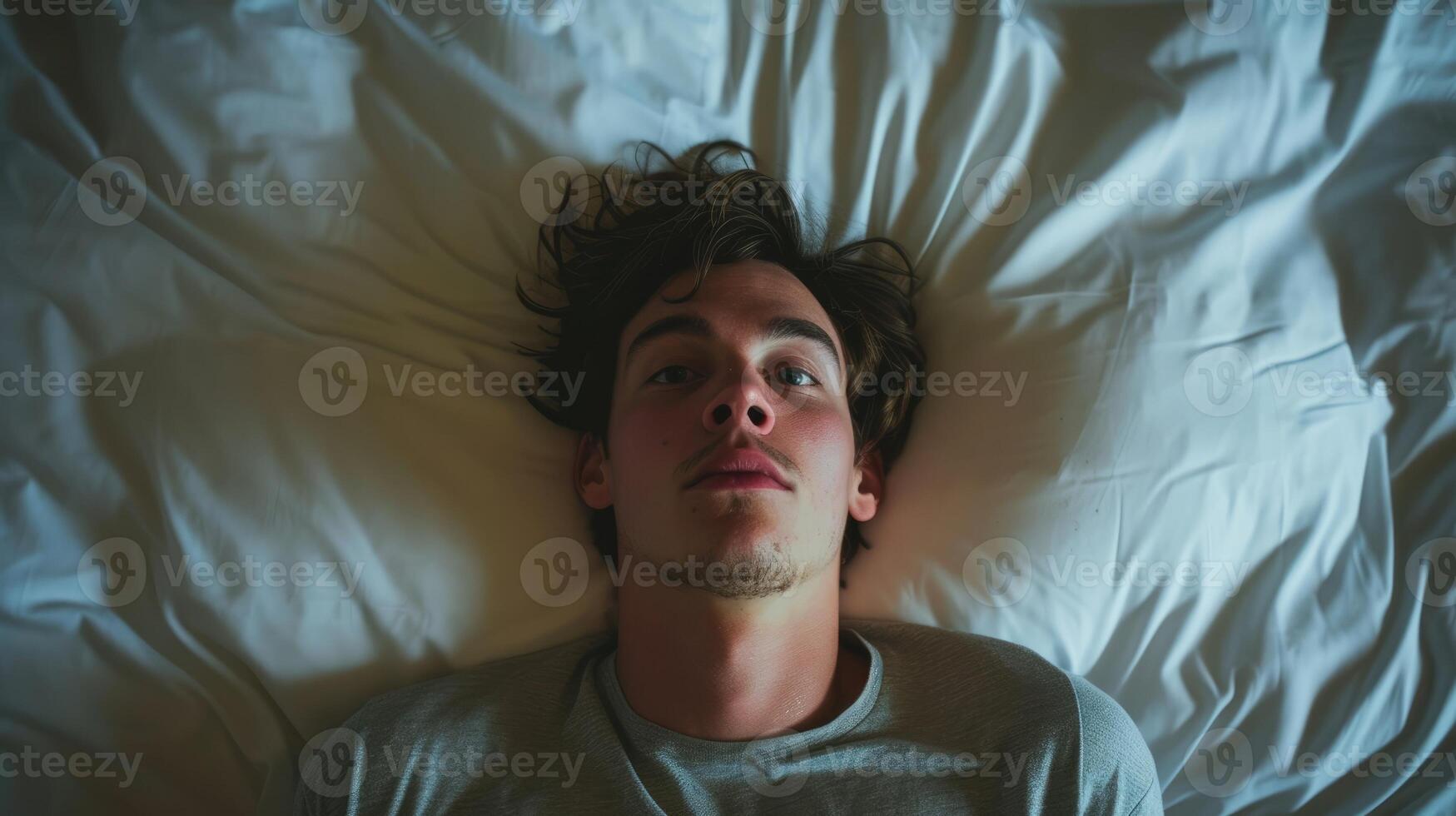 A young man lying in bed staring up at the ceiling with a broken look on his face photo