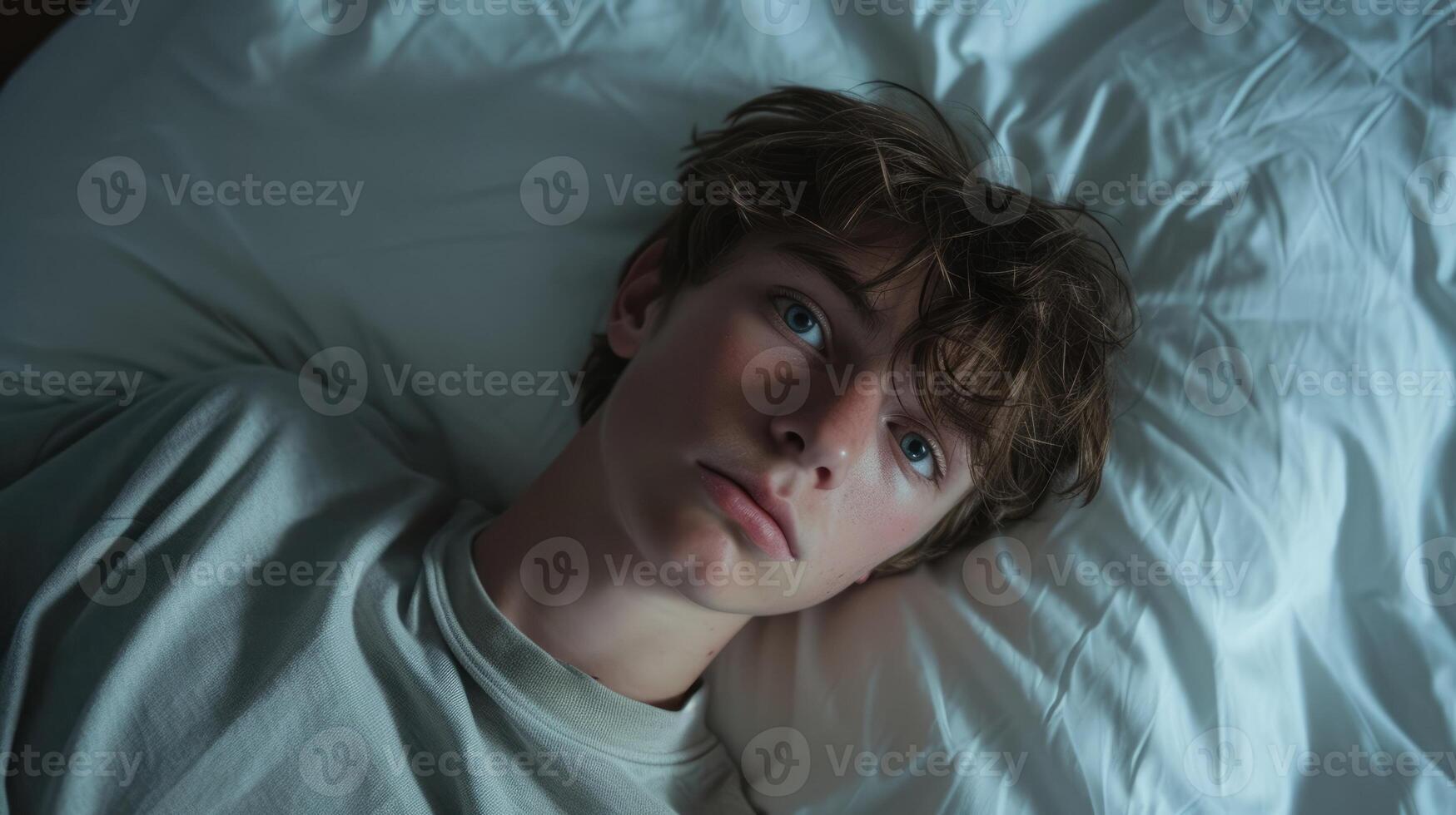 A teenage boy lies on his bed staring at the ceiling with a look of frustration photo