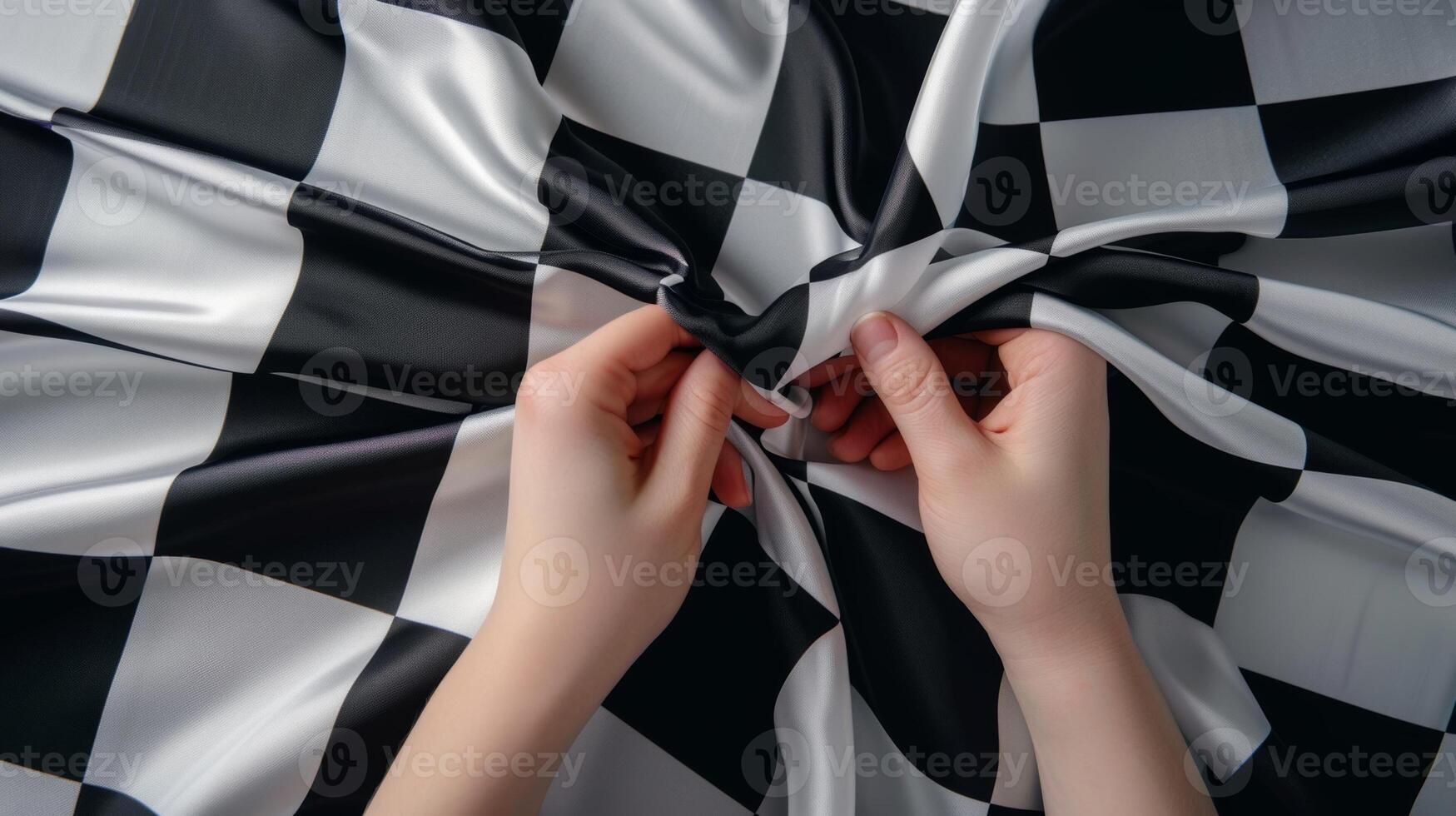 A pair of hands carefully unfolding a checkered flag revealing its iconic black and white pattern. The fabric is smooth and crisp to the touch indicating its quality photo