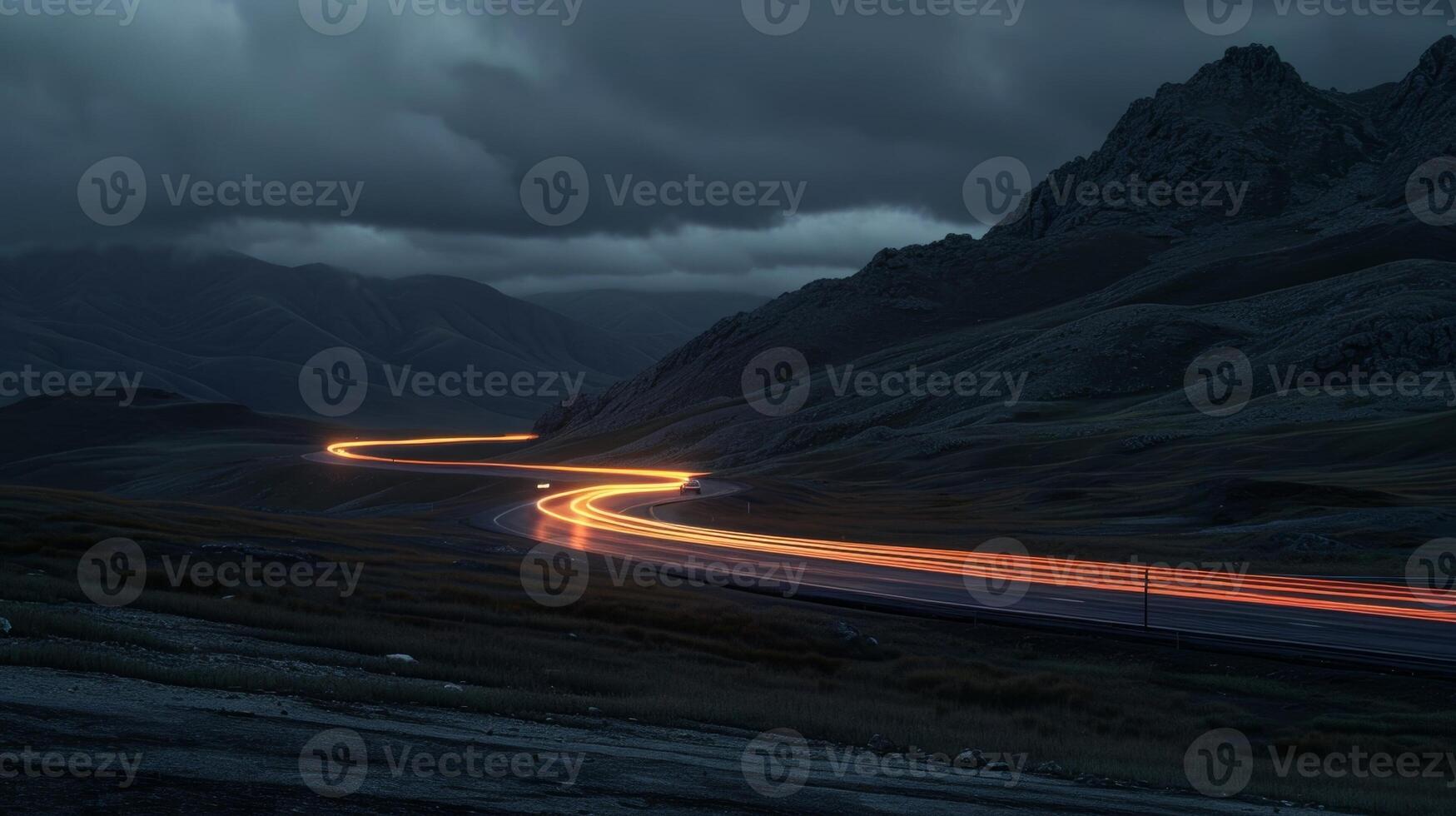 A solitary car making its way along the mountain road with the headlights creating a trail of light in the darkness photo