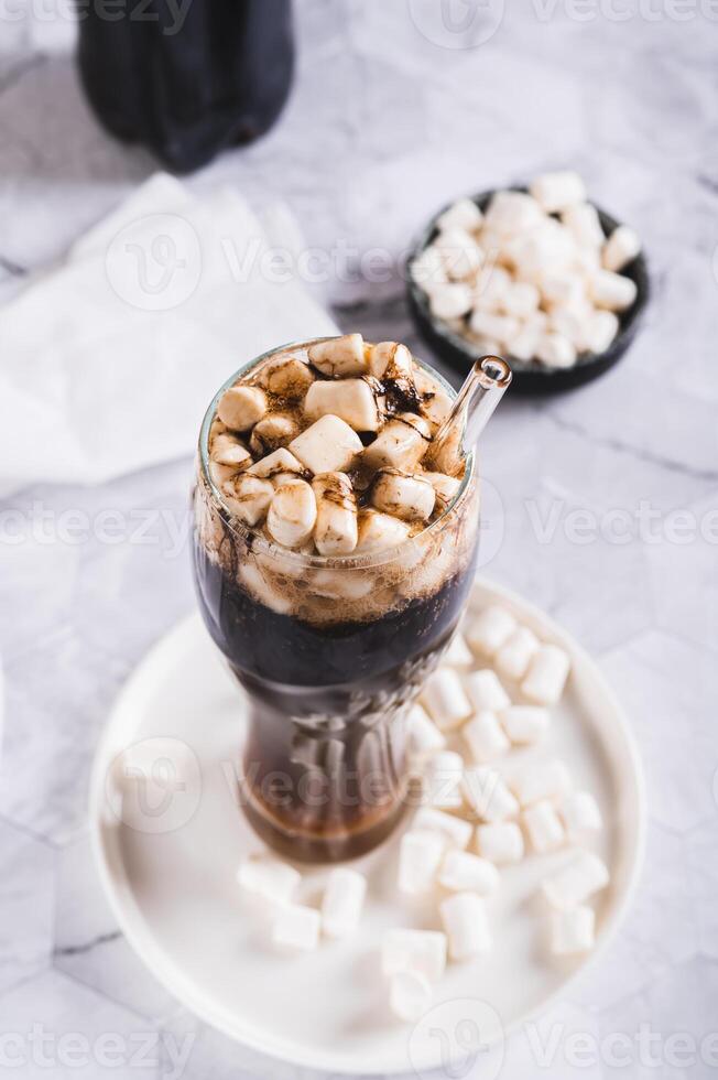 Refreshing fluffy coke with marshmallow in a glass on the table vertical view photo