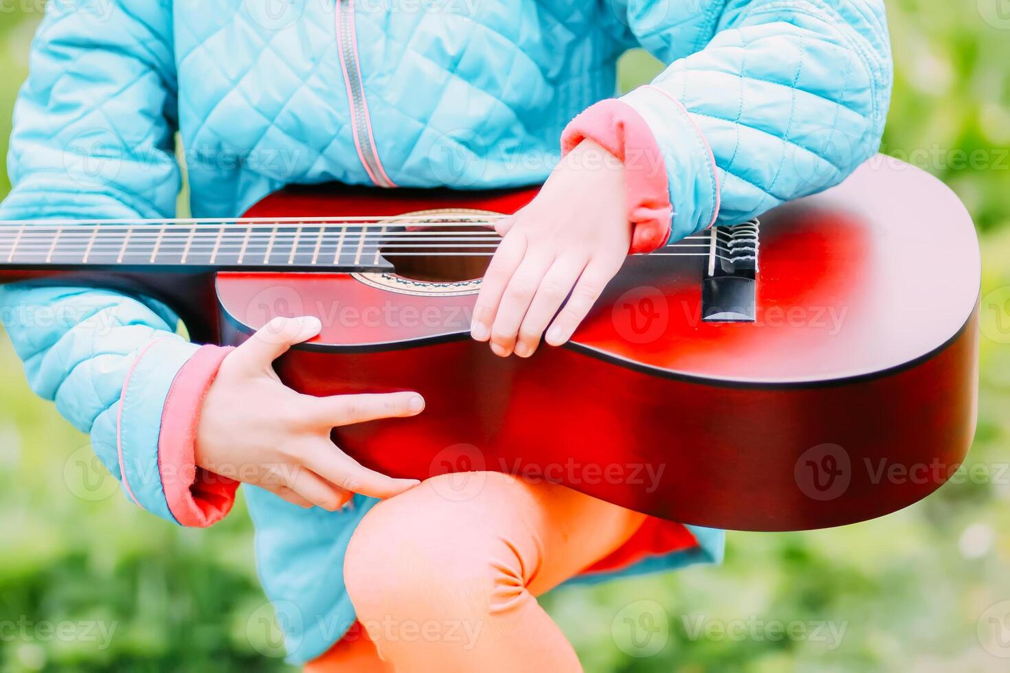 Little girl playing guitar and singing outdoors on green meadow at spring. Happy child with musical instrument on rural yard. photo