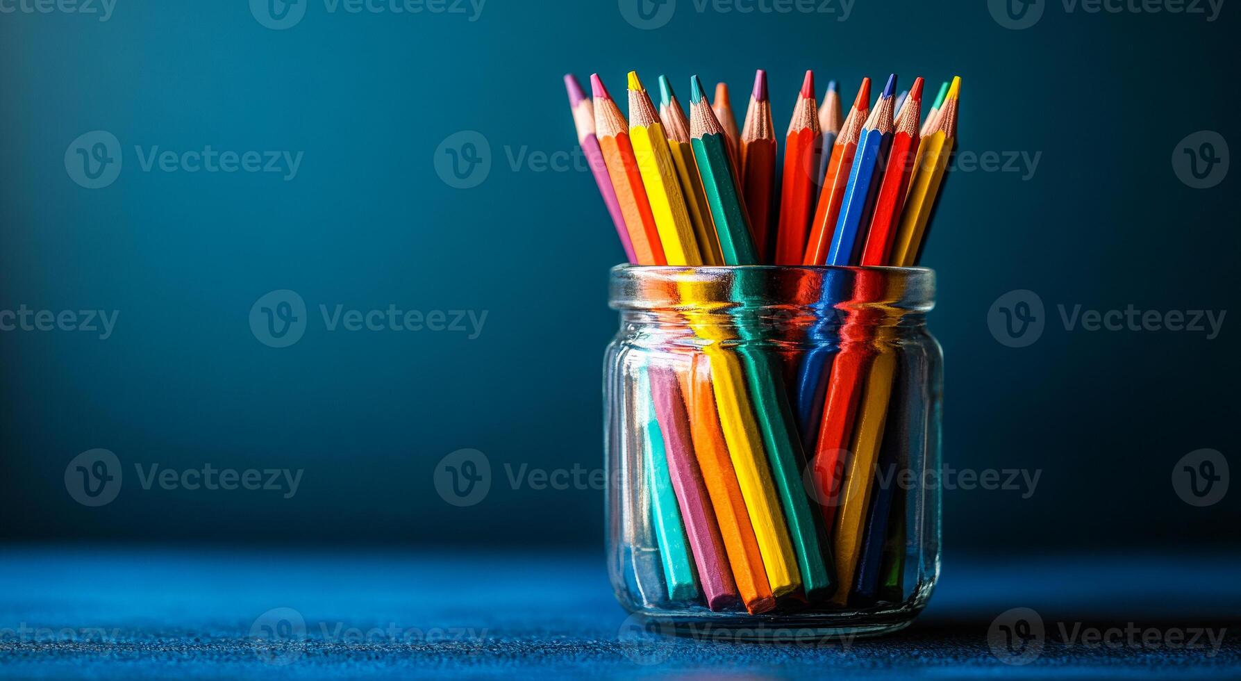 A jar full of colored pencils on a blue background. The pencils are of different colors and are arranged in a neat manner. The jar is placed on a table photo