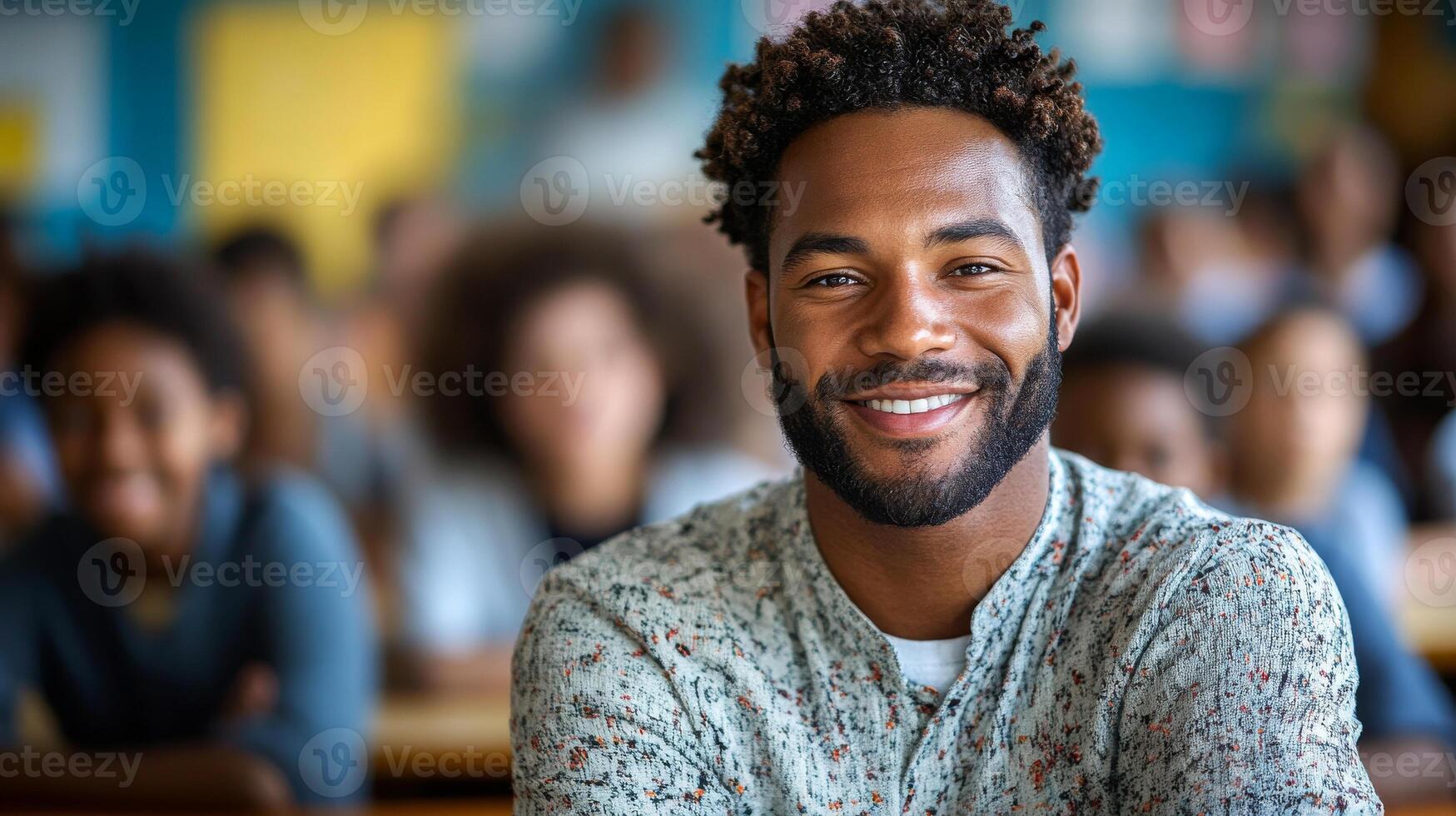 A man with a beard and a smile is sitting in a classroom with other people. He is the center of attention and he is happy photo