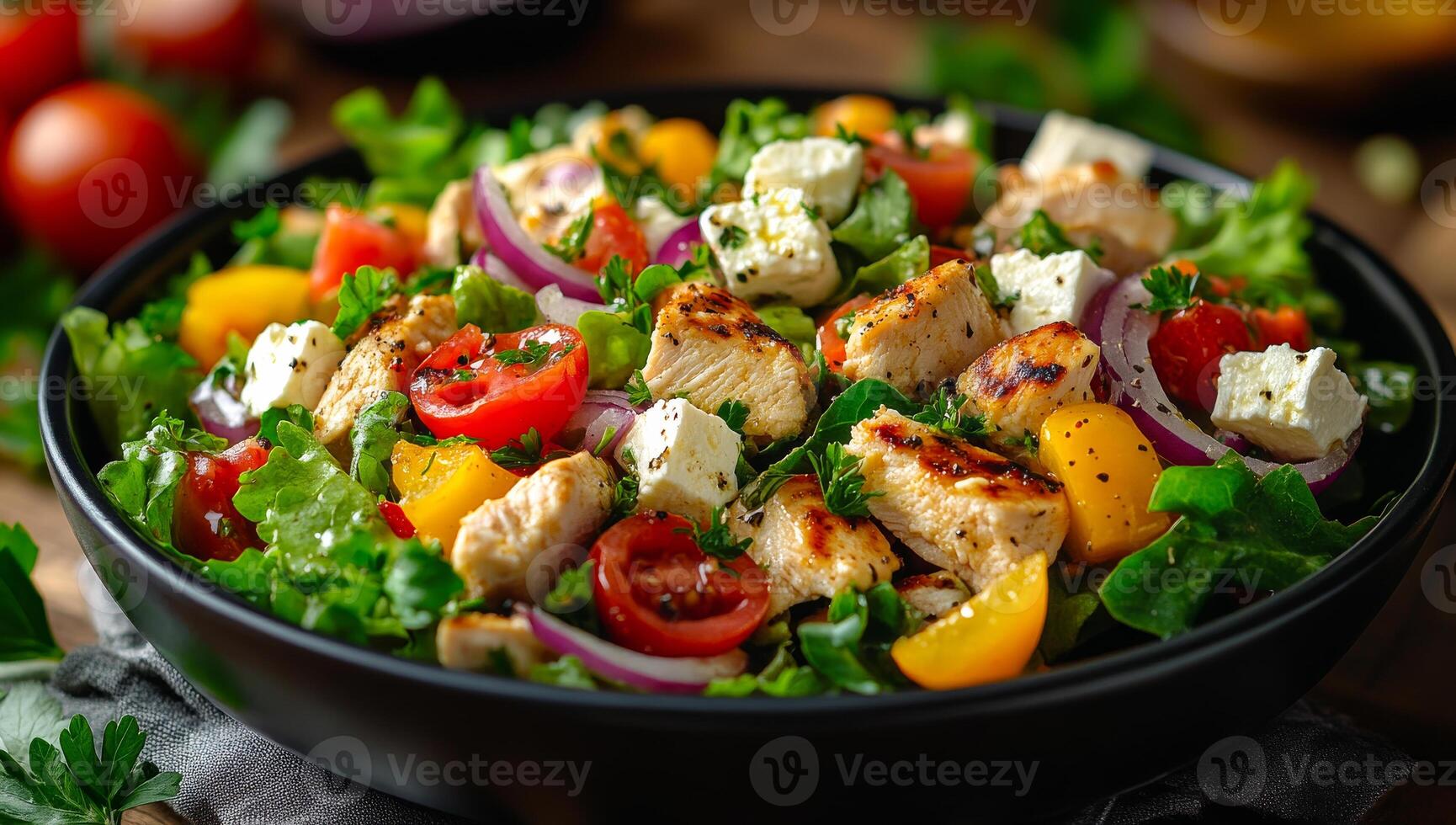 A black bowl filled with a salad of chicken, tomatoes, and onions. The salad is served on a wooden table photo