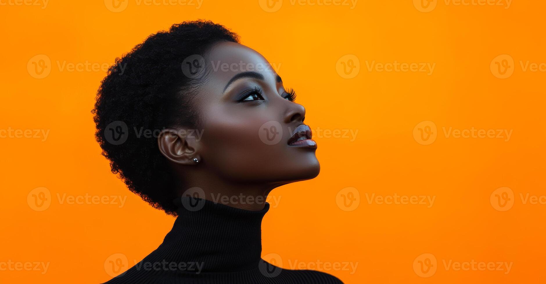 A woman with a short haircut and a black sweater is looking at the camera. The orange background adds a warm and inviting atmosphere to the image photo