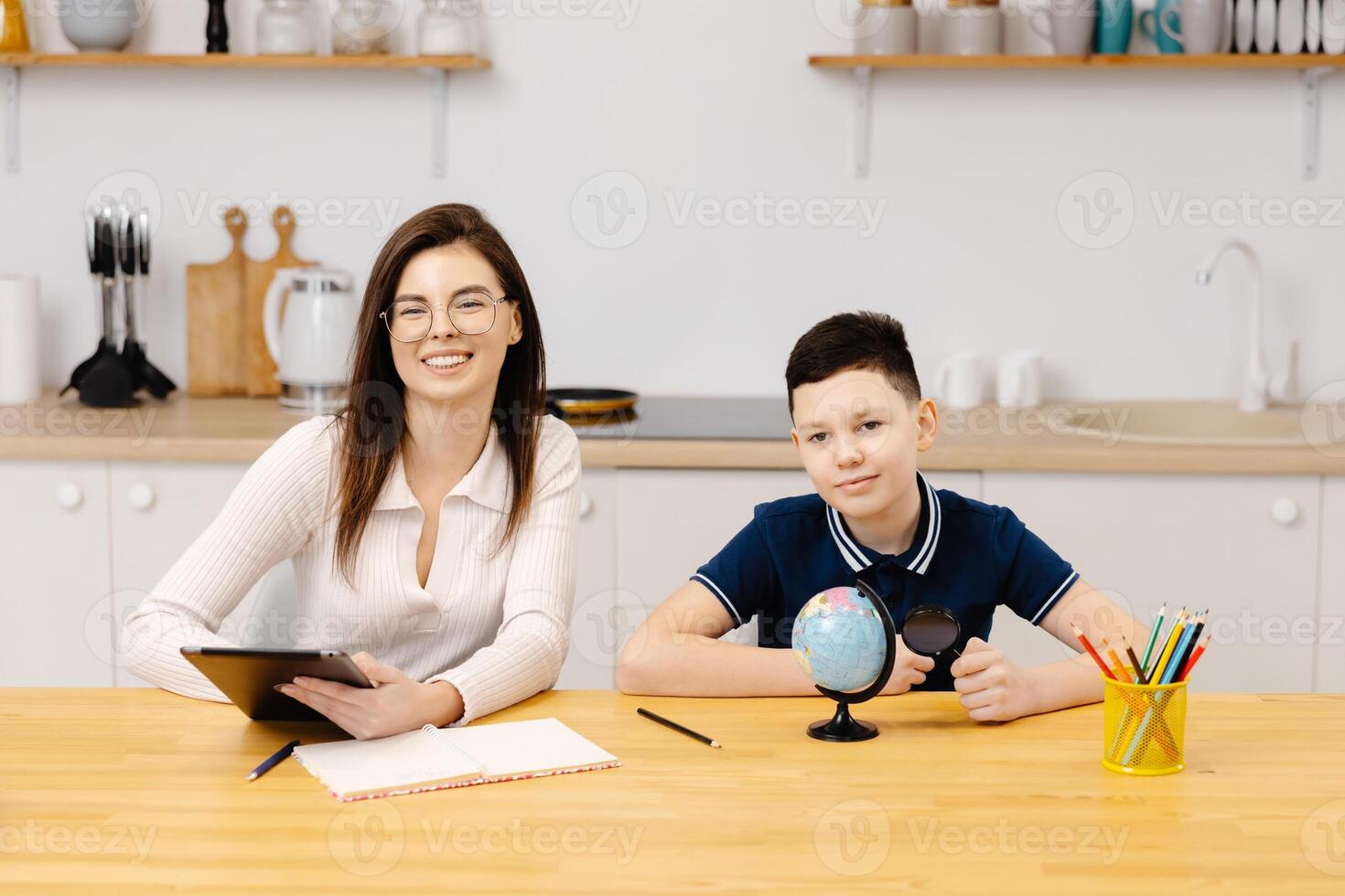 A young woman helps a boy with his lessons using a tablet and a globe. A homeschooling student does his homework with the help of a tutor photo
