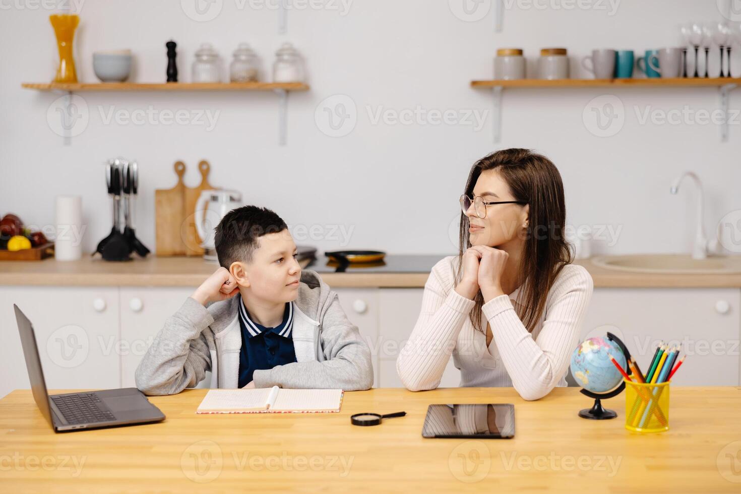A young woman helps a boy with his lessons using a tablet and a globe. A homeschooling student does his homework with the help of a tutor photo