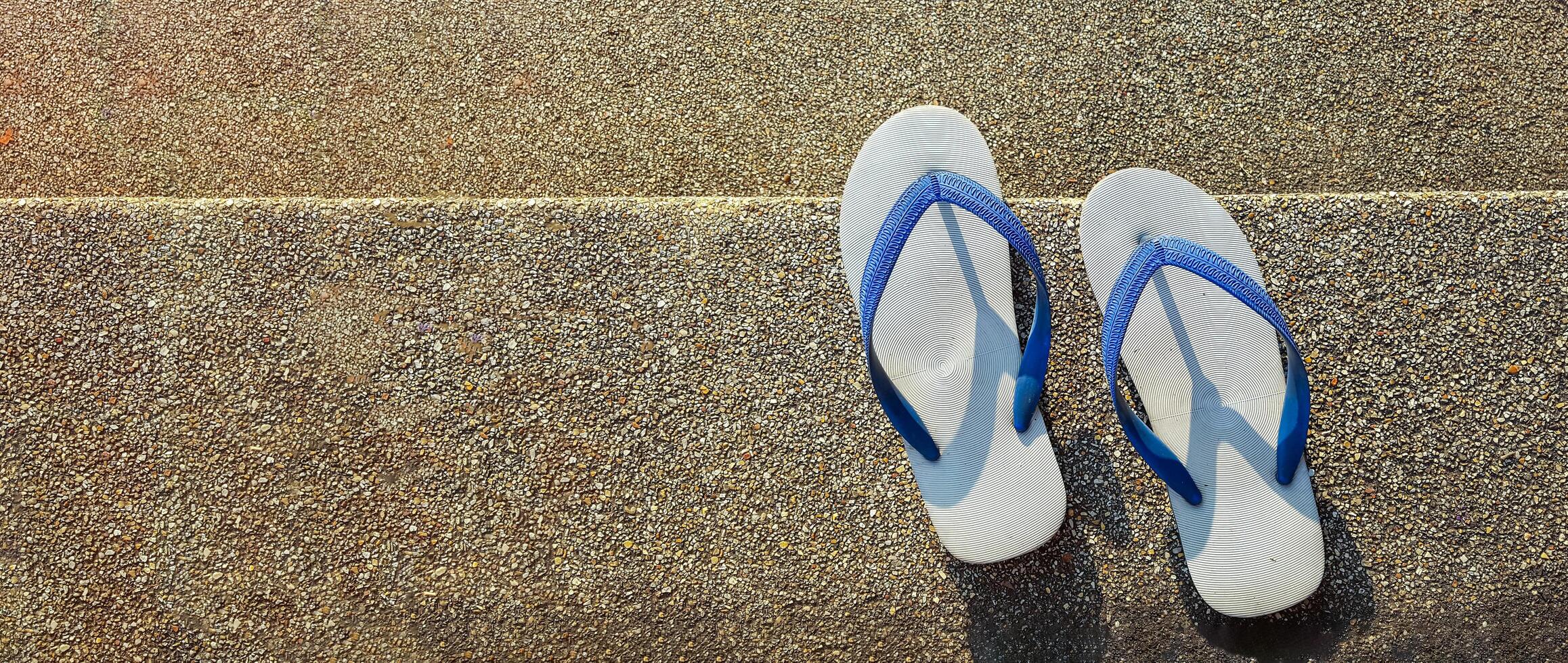 A pair of white rubber flip flops with blue straps neatly placed on a rough stone staircase, representing the concept of relaxation and travel, evoking a sense of comfort, and outdoor exploration. photo
