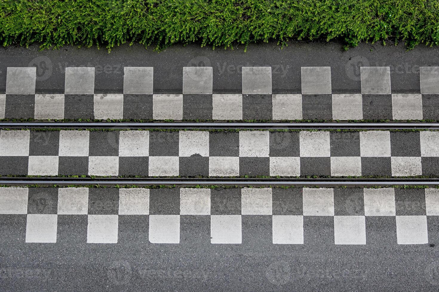Directly above view of tram tracks running between rows of checkered tiles, bordered by greens photo