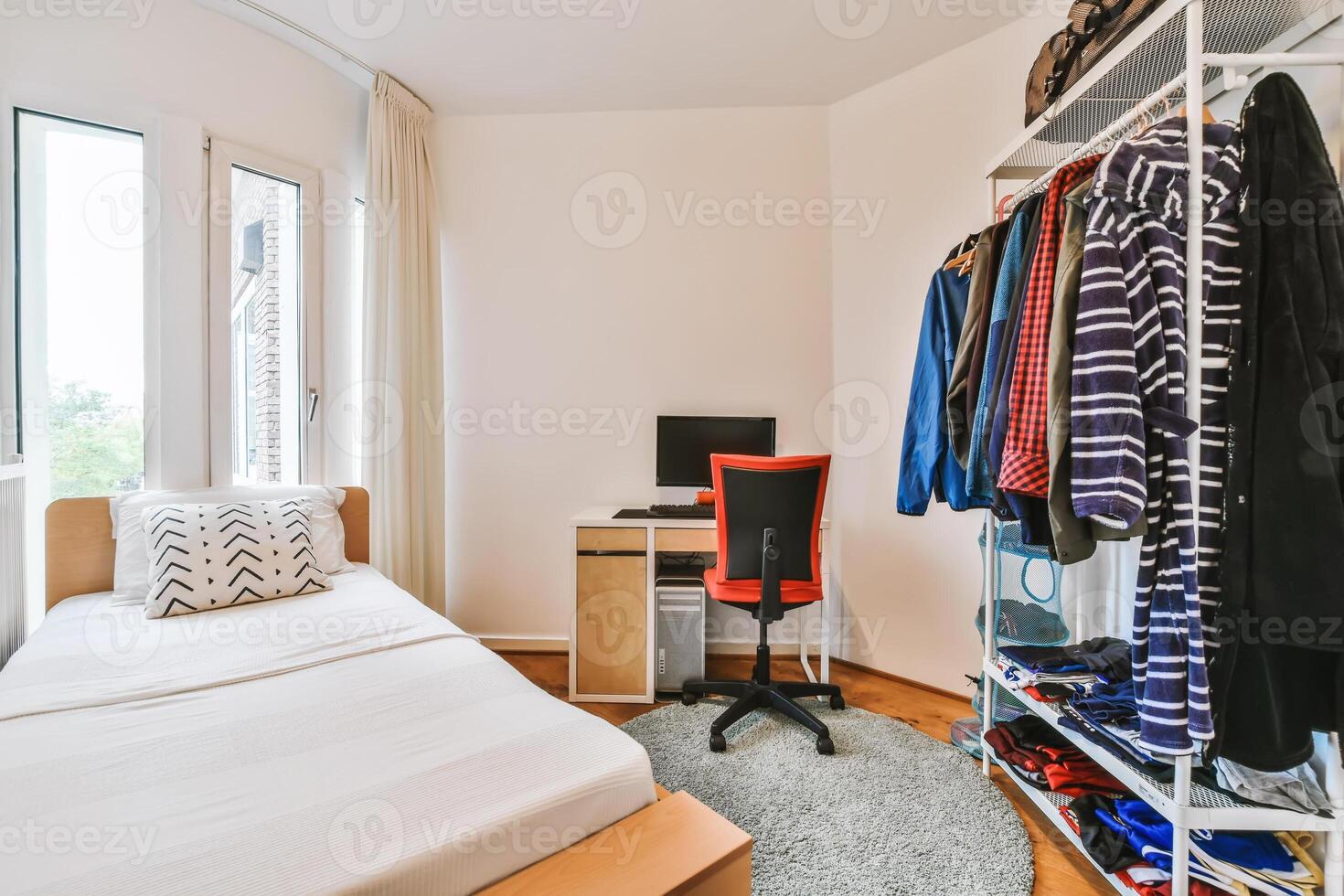 A bedroom with a bed, desk and clothes rack photo