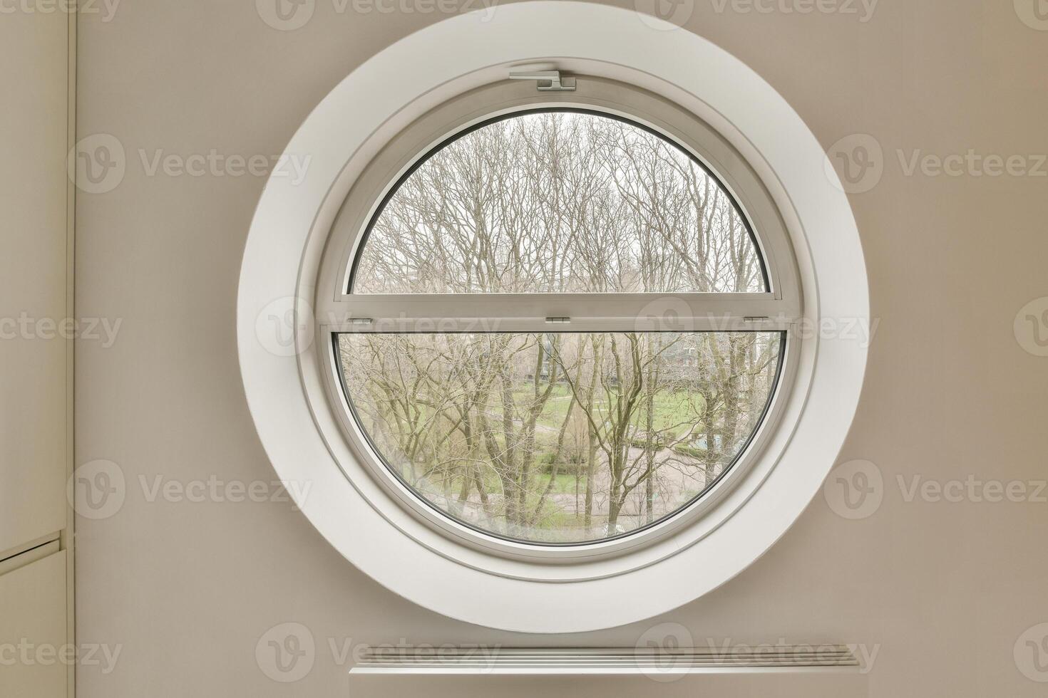 A round window in a white wall with a view of trees photo