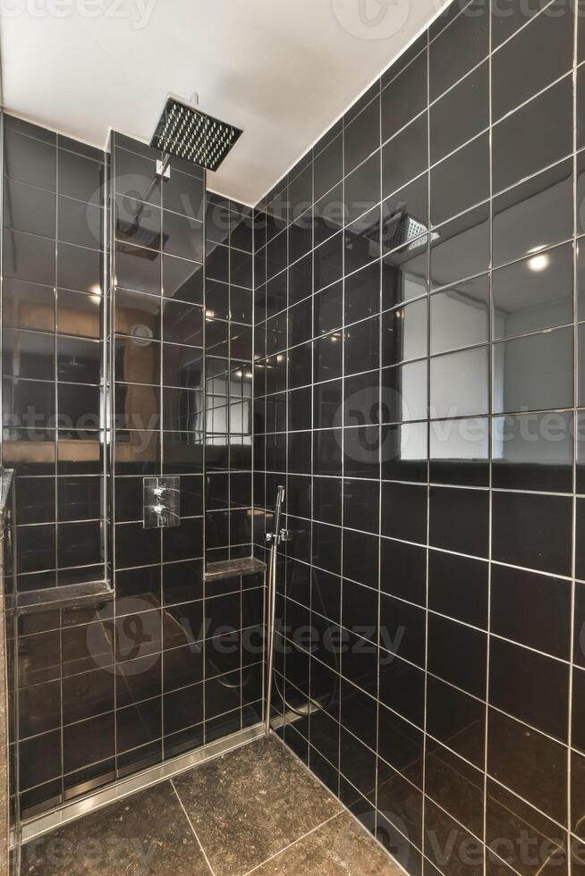 A shower with black tile walls and floor photo