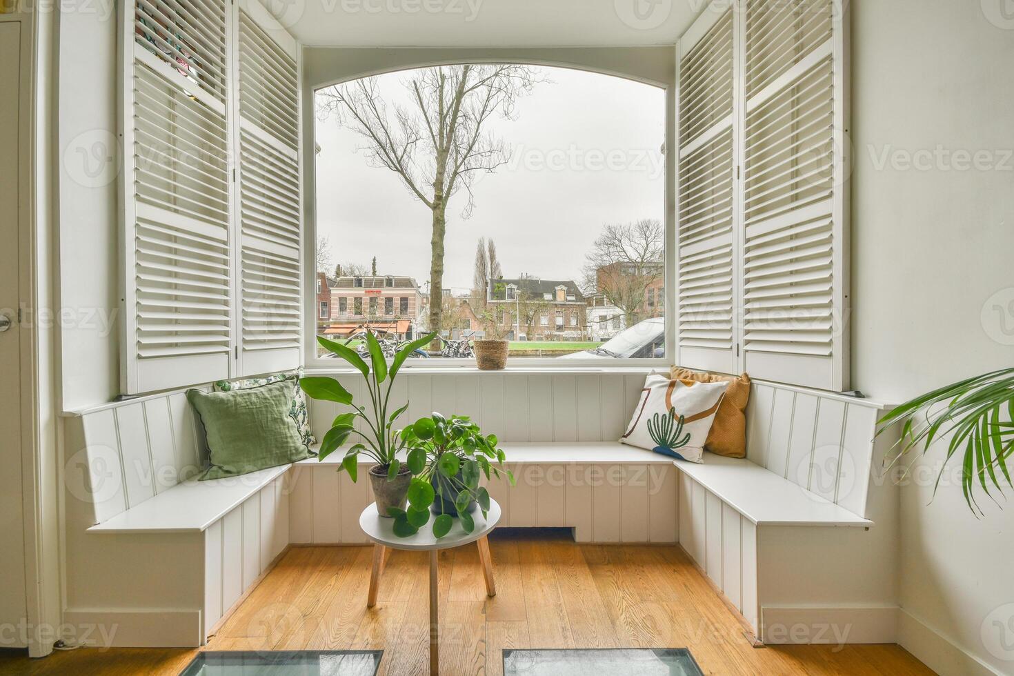 A window seat with white shutters and a plant on the floor photo