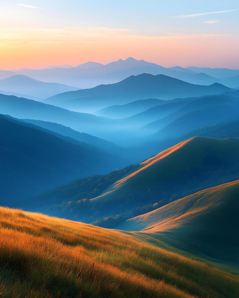 Landscape of majestic mountain ranges at sunrise, with golden sunlight casting soft rays over distant hills and valleys. The foreground consists of a grassy ridge covered in golden autumn hues. photo