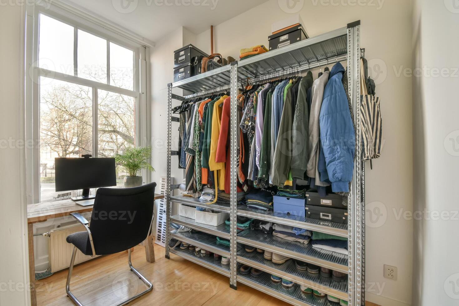 A room with a desk, clothes rack and window photo