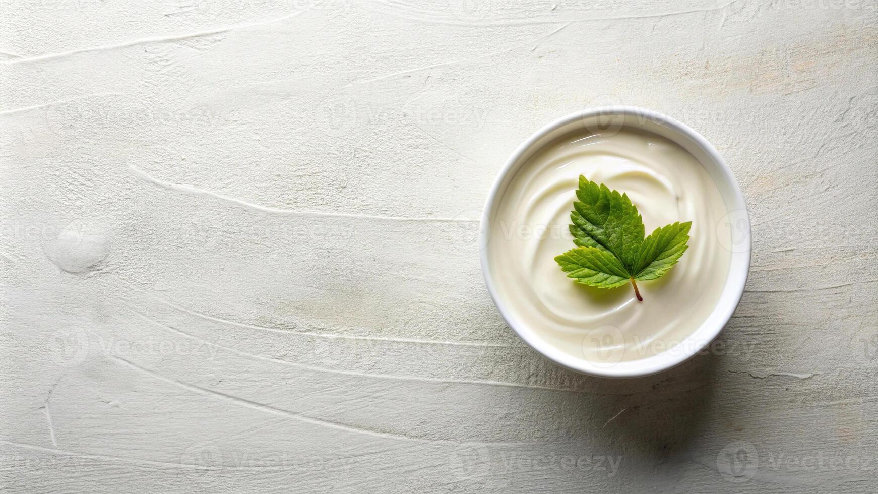 A table set with a bowl of cream, a sheet of paper, and a leaf viewed from above photo