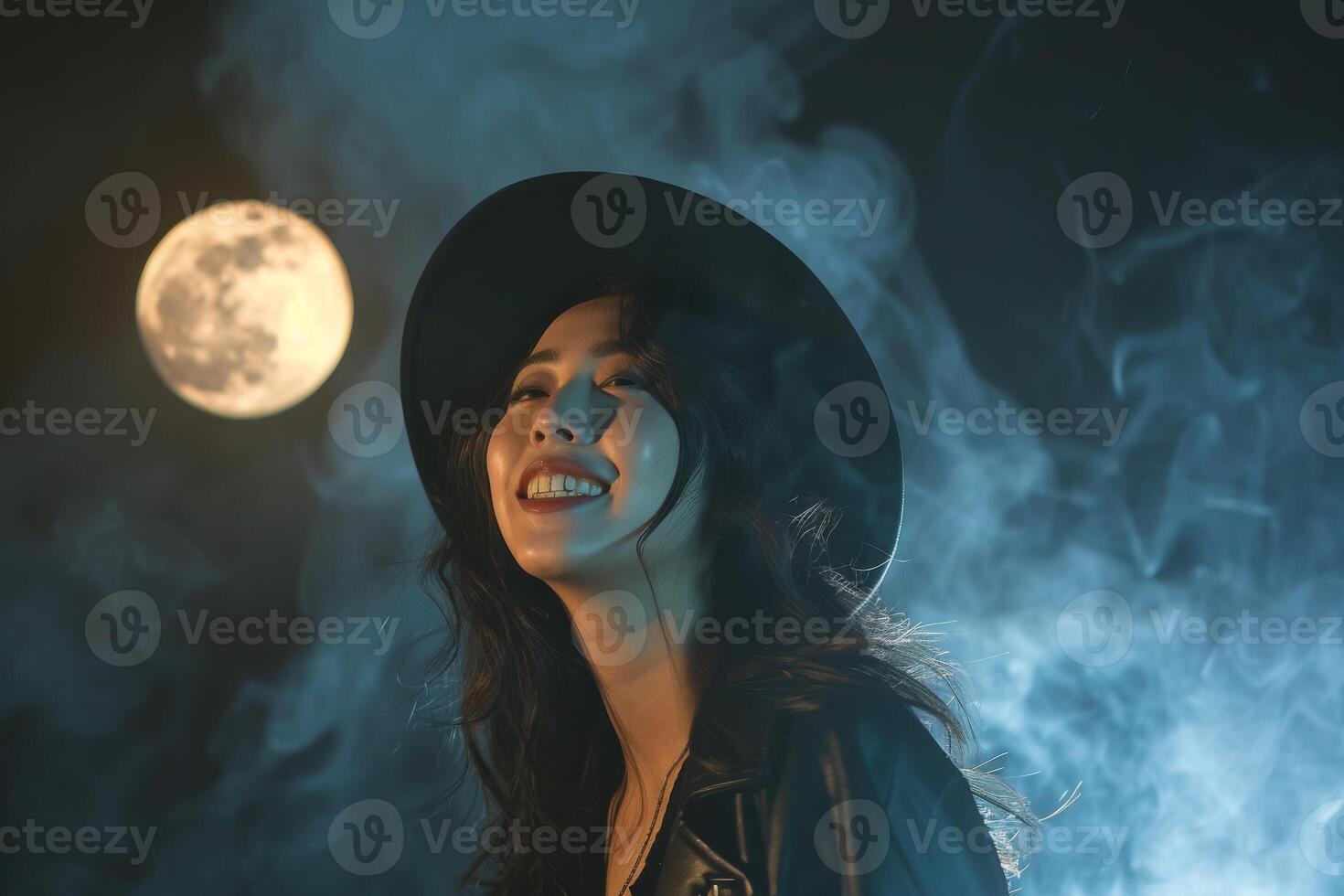 A woman in a hat and black jacket is smiling while standing in front of a full moon photo