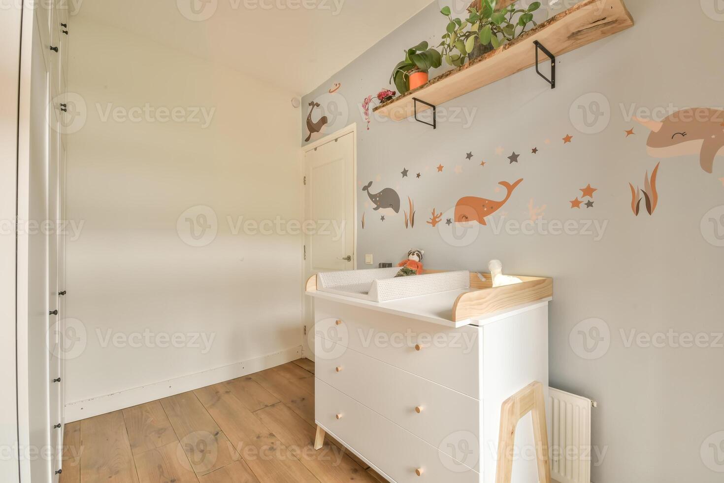 A small nursery room with a wooden floor and a white dresser photo