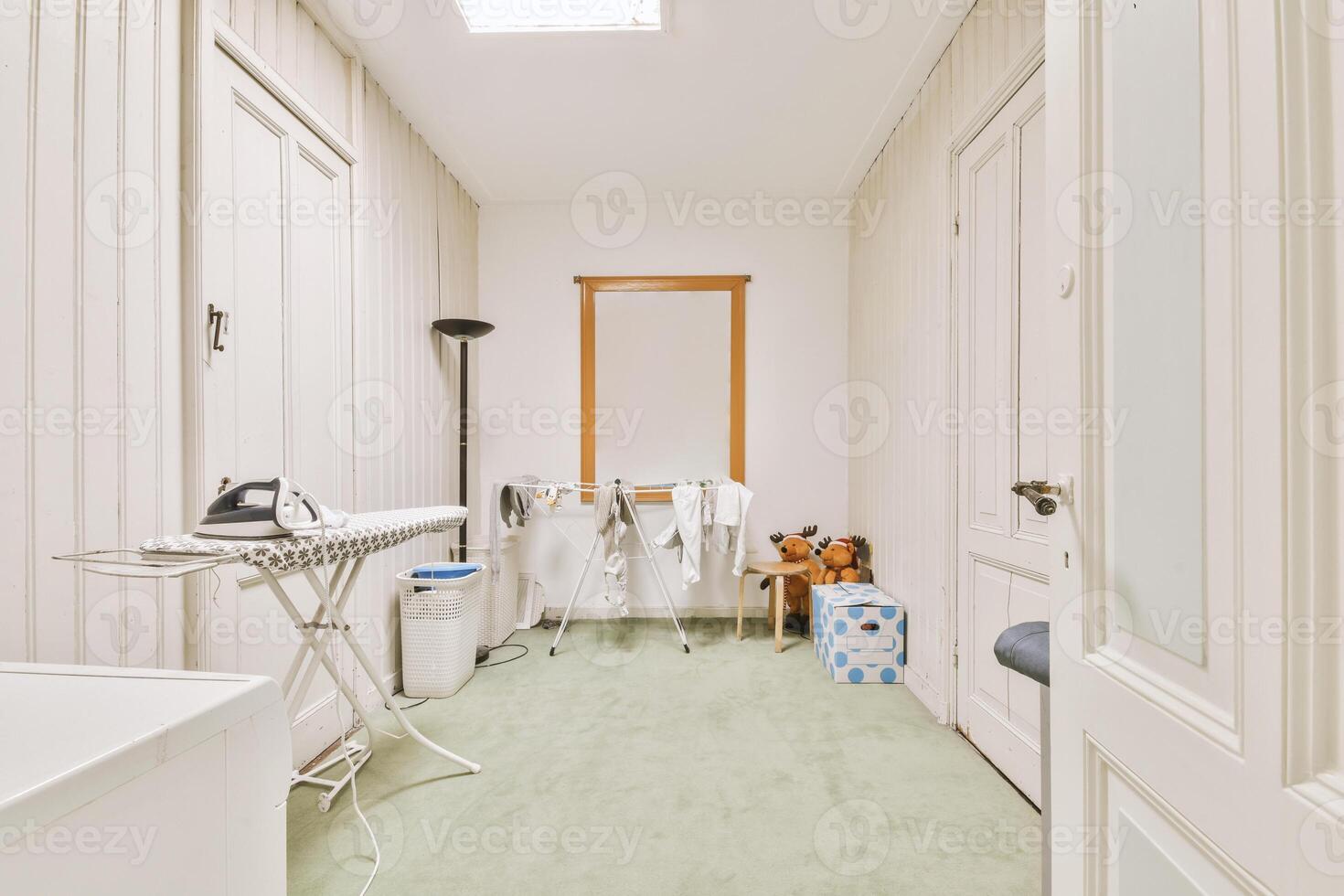 A laundry room with a washing machine, ironing board and a teddy bear photo