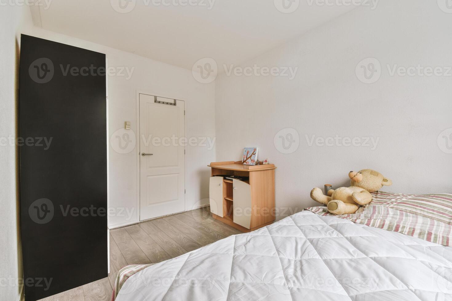 A small bedroom with a teddy bear sitting on the bed photo