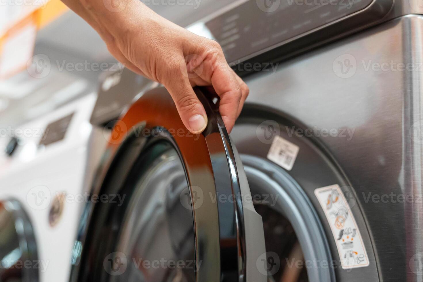 A hand reaches out to open a modern washing machine door photo
