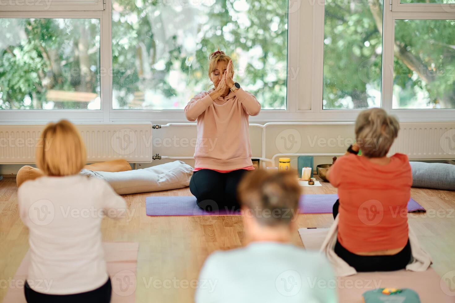 A group of senior women engage in various yoga exercises, including neck, back, and leg stretches, under the guidance of a trainer in a sunlit space, promoting well-being and harmony photo