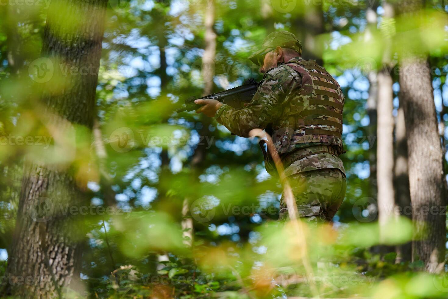 An elite soldier, camouflaged and stealthily navigating through dangerous woodland terrain, executes a covert mission in a secluded forest area photo