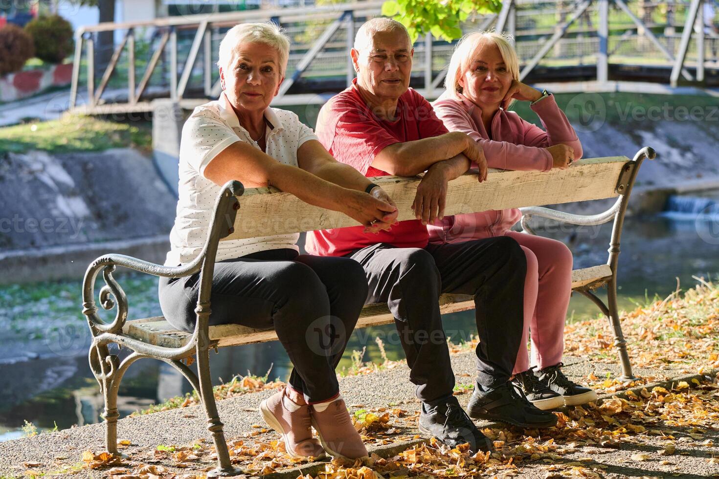 A group of elderly individuals, including a senior man and two older women, sits in a park on a sunny autumn day, embodying the concept of healthy aging through companionship, relaxation, and outdoor photo